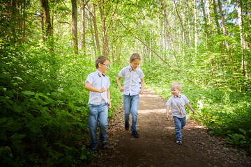 Boys in a white shirts and a pink butterfly in nature among the greenery. Funny walk of three brothers in the park or forest