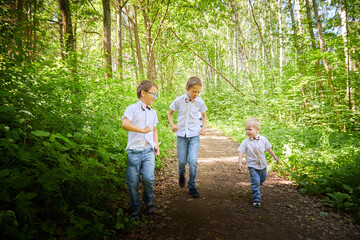 Fototapeta premium Boys in a white shirts and a pink butterfly in nature among the greenery. Funny walk of three brothers in the park or forest