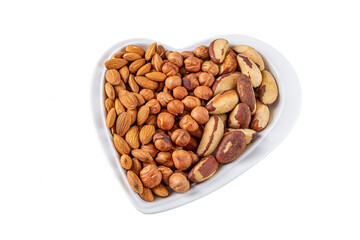 Assortment of various types of nuts - hazelnuts,  almonds, pecan in heart shaped plate isolated on white background. Healthy vegetarian snacks. Protein-containing food. Flat lay, Copy space for text.