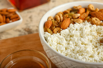 Bowl of cottage cheese with peanuts and cornflakes on wooden board, closeup