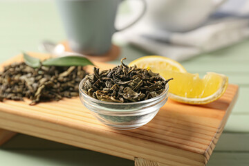 Bowl of dry green tea leaves on wooden stand, closeup