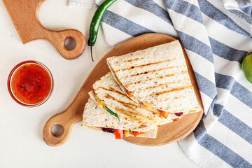 Board with tasty vegetarian quesadillas and sauce on white background
