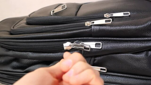 Close-up of a black leather bag with many zippers and a mans hand fastening one of them. Vertical video for a social media story