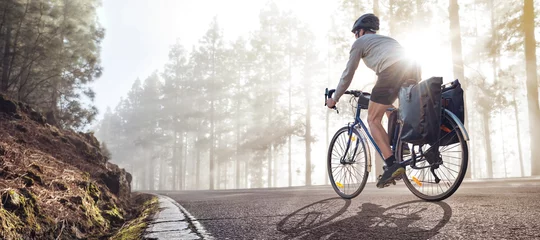 Poster Cyclist on a bicycle with panniers riding along a foggy forest road © photoschmidt