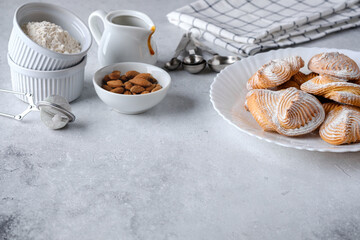 Cookies on a plate with powdered sugar after the cooking process. Metallic kitchen strainer, napkin, almond, measuring spoons, caramel sauce and flour next to it. Copy space.