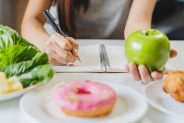 Diet, Dieting asian young woman working, write diet plan right nutrition, hold green apple, vegetables salad is food for good health not choose eat donut, junk food. Nutritionist, Weight loss person.