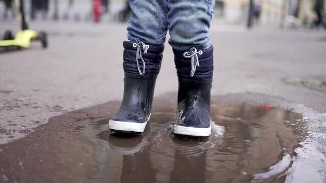 Happy child jumping into puddle of water. Joyful kid bouncing in water puddle