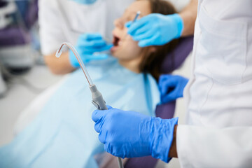 Close-up of dentist using dental suction tube during appointment with patient at dentist's office.