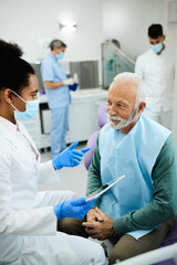 Smiling mature man communicating with African American dentist during appointment at dental clinic.