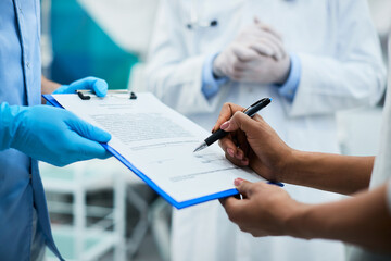 Close-up of patient signing medical form before dental procedure at dentist's office.