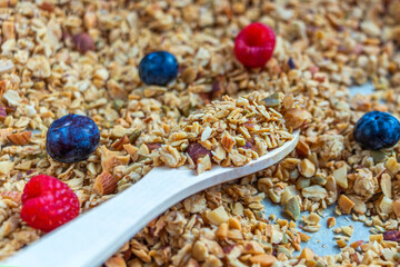 Freshly baked granola, muesli from oat flakes, varius of nuts, honey, pumpkin seeds on baking sheet decorated with berries. Home cooking healthy vegetarian snack. Homemade food concept. Keto diet.