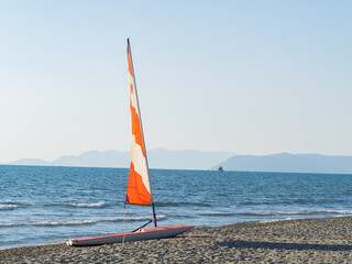 small sailing  boat with orange-white  striped sail - 428091824