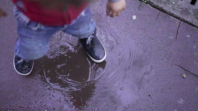 Happy child jumping into puddle of water. Joyful kid bouncing in water puddle