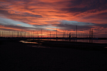 Silhouetted sailboats on orange color seascape over sunset sky.	