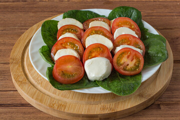 caprese salad in a white plate on a wooden table.