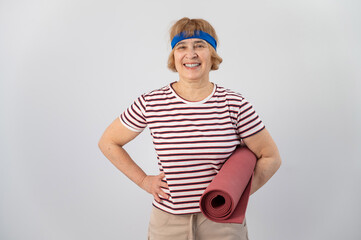 Elderly caucasian woman holding folded yoga mat in studio.