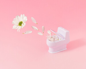 Trendy composition with toilet bowl full of petals and white daisy flower on pastel pink background.