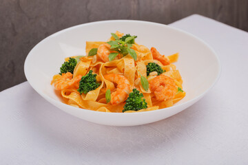 A view of dish of Tagliatelle pasta with broccoli, toasted pine nuts and shrimps on white plate. Creative isometric style. Mediterranean cuisine.
