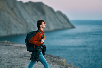 Traveling with a backpack in the mountains outdoors looking at the sea red sweater jeans model