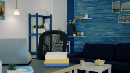 Office living room with nobody in it, place of home work, workplace indoors concept with open laptop on desk. Interior of empty bright workspace with blue furniture and walls, beautiful decorated.