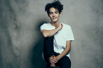 cute guy with curly hair in a white t-shirt sits on chairs studio fashion