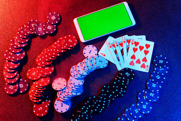 The concept of an online casino: playing cards, betting chips and a smartphone with a copy space and a green background. Top view.