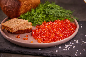 Delicious red caviar in a plate on the table, dark background. A beautiful and hearty dinner with red caviar. seafood and seafood delicacies