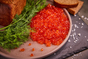 Delicious red caviar in a plate on the table, dark background. A beautiful and hearty dinner with red caviar. seafood and seafood delicacies