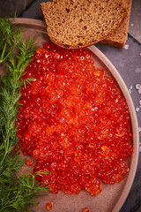 Delicious red caviar in a plate on the table, top view, dark background. A beautiful and rich dinner with red caviar. seafood and seafood delicacies