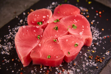 A fresh raw tuna steak sits on a black table with thyme. There is sea salt around the tuna
