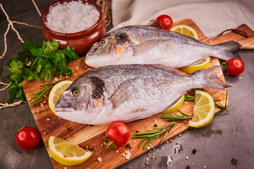 Fresh raw dorado fish. Sea bream, lying on a wooden board on a gray table with herbs and salt and spices. Dorado and ingredients for cooking on the table. Top view