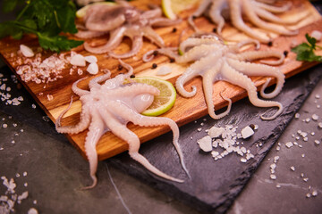 Small octopus tentacles on a wooden board on a black table. Octopus on the kitchen table with herbs and lemon. The concept of healthy seafood food