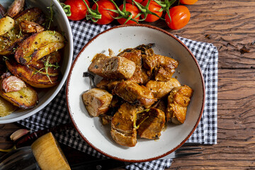 Appetizing stew of pork tenderloin meat cooked in the wok, cut into cubes. With roasted and golden potatoes, garlic, salt, oregano and fresh tomatoes. Homemade look. Top view.