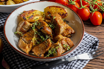 Appetizing stew of pork tenderloin meat cooked in the wok, cut into cubes. With roasted and golden potatoes, garlic, salt, oregano and fresh tomatoes. Homemade look. Close-up