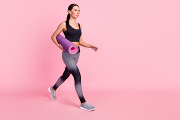 Fototapeta na wymiar Photo of pretty charming young lady sportswear running fast holding yoga mat looking empty space isolated pink color background