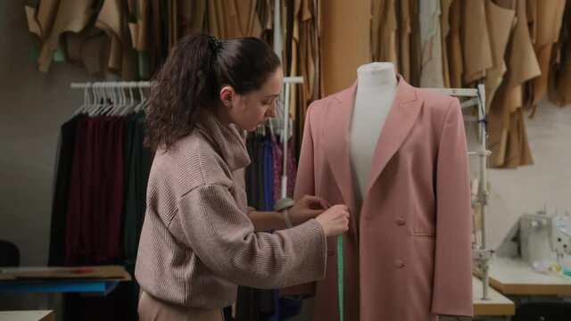 female tailoring fashion designer measuring suit jackets on mannequin dummy in workshop studio atelier. Small handmade business