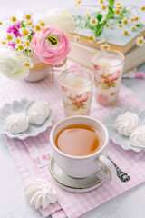 Fototapeta na wymiar Cup of tea, small meringue cookies and books with beautiful tender blossoming of fresh cut bouquet in background