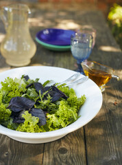 Fresh salad mix of arugula leaves, basil, and lambs lettuce. Salad bowl, healthy food. Composition in a white plate on an old wooden table