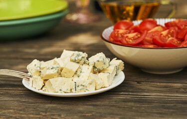 Blue cheese on wooden background. Plate with tomatoes in the background
