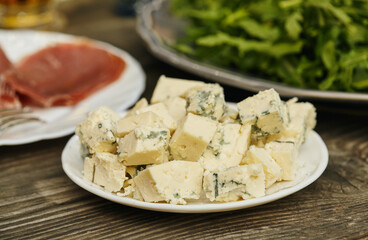 Blue cheese on wooden background. Prosciutto and arugula in the background