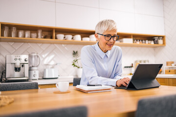 Portrait of a senior woman using tablet while sitting in the kitchen.