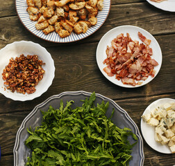 Ingredients for arugula salad, blue cheese, prosciutto, pear and caramelized nuts on an old table. Top view