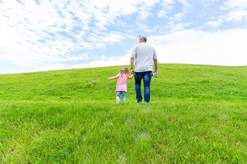 Naklejka na ściany i meble dad and little daughter walk by the hand up the mountain, beautiful sky. paternity concept