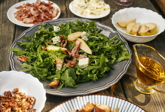 Ingredients for arugula salad, blue cheese, prosciutto, pear and caramelized nuts on an old table. Top view