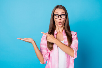Photo of excited lady palm hold empty space direct finger wear glasses pink striped shirt isolated...