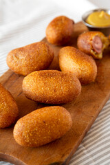 Homemade Mini Corn Dogs on a rustic wooden board on cloth, side view.