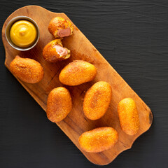 Homemade Mini Corn Dogs on a rustic wooden board on a black background, top view. Flat lay,...