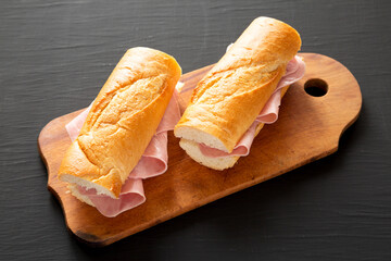Homemade Parisian Jambon-Beurre Sandwich on a rustic wooden board on a black surface, side view.