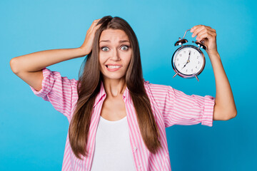 Photo of crazy nervous lady hand head hold alarm clock wear pink striped shirt isolated blue...