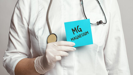 Cropped view of doctor in a white coat and sterile gloves holding a note with text - MAGNESIUM - obrazy, fototapety, plakaty